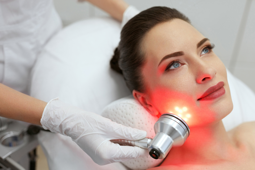 Facial Beauty Treatment. Woman Doing Red Led Light Therapy On Face Skin At Cosmetology Center. High Resolution