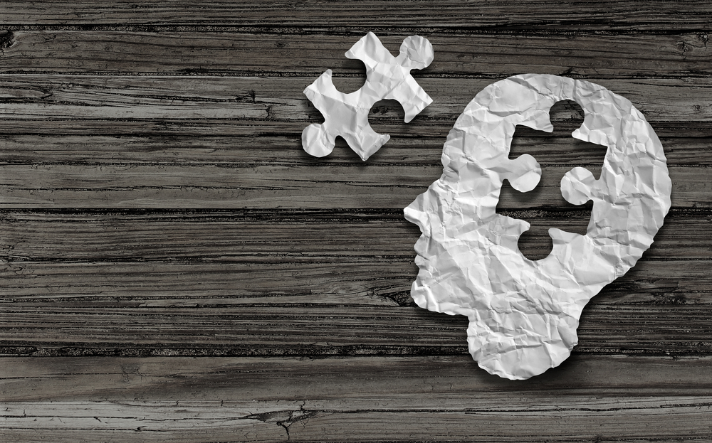 Mental health symbol Puzzle and head brain concept as a human face profile made from crumpled white paper with a jigsaw piece cut out on a rustic old double page spread horizontal wood background.